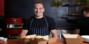 Smiling chef serving takeaway burgers using Angel Bay patties.