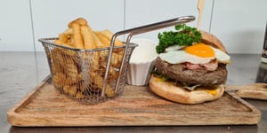 Angel Bay patty on burger with bacon and egg alongside serving of fries.